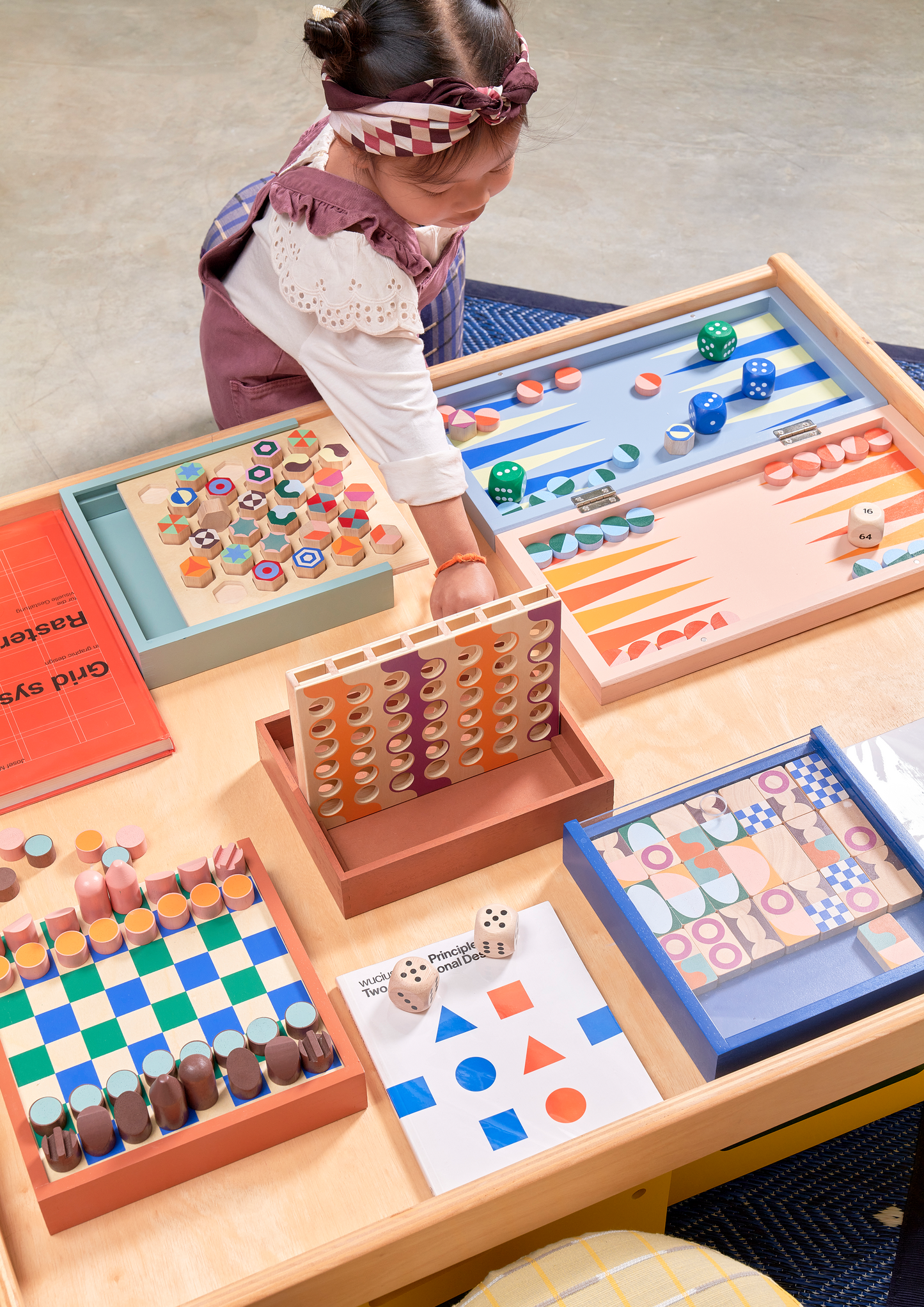 A set of multicolored geometric pattern dominoes pieces arranged in a line on a blue tray, with a wooden case in the background.