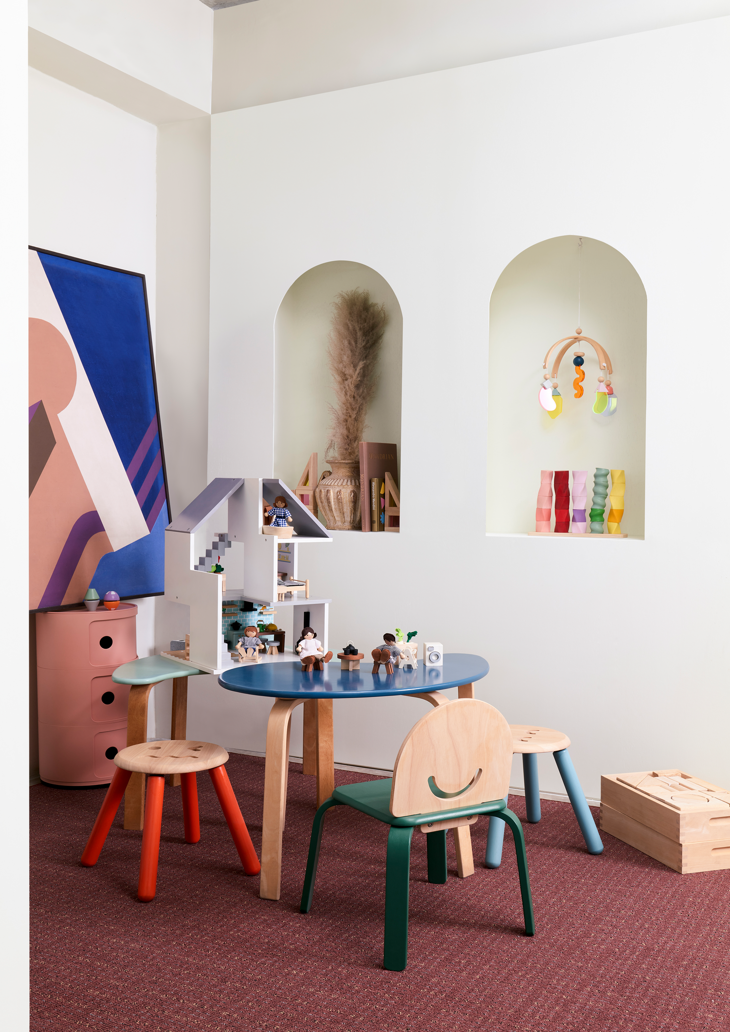 A set of colorful geometric shape sorters on a wooden board. The sorters are in shapes of a sphere, cube, cylinder, cone, and rectangular prism, each a different color.