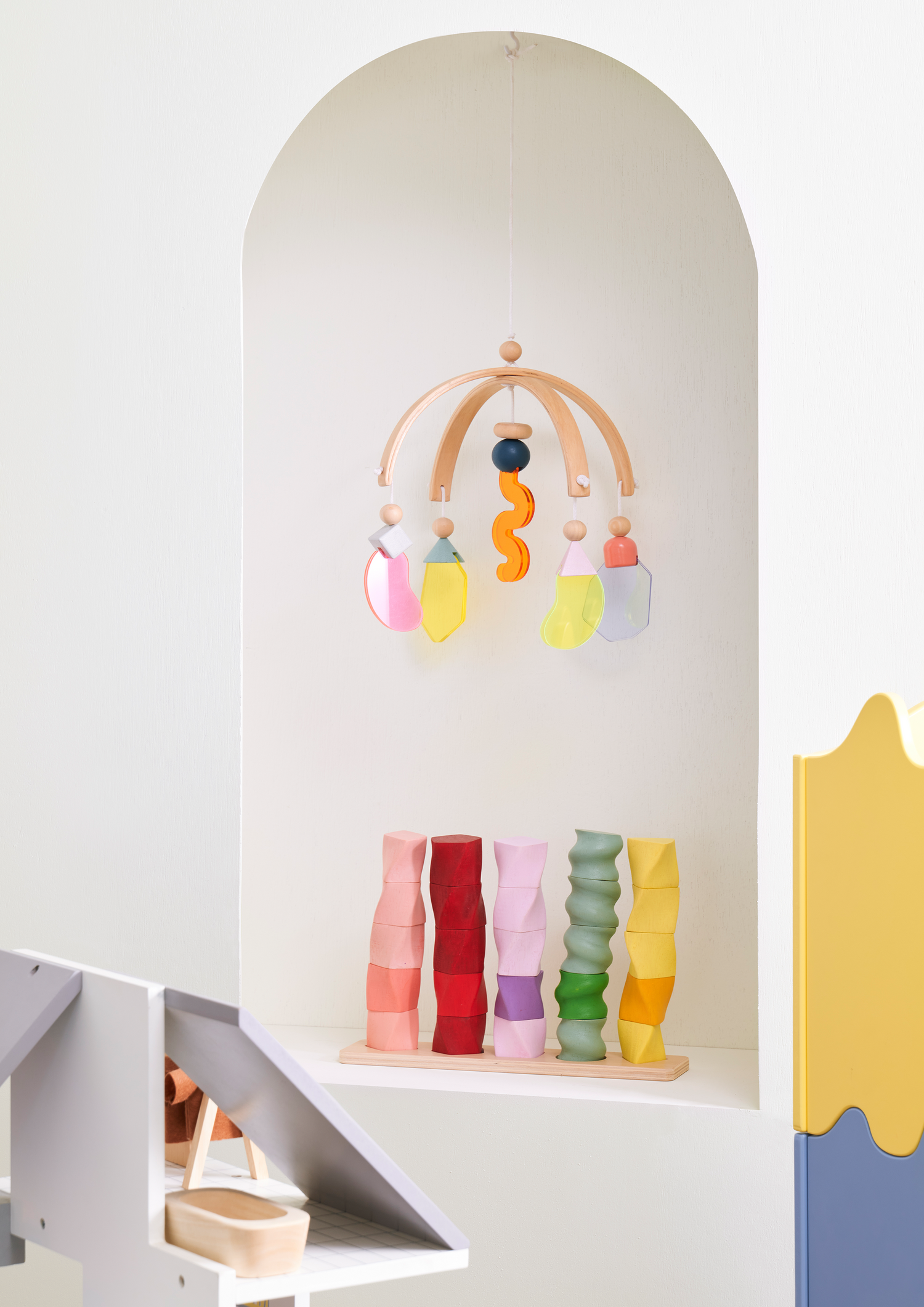A set of colorful geometric shape sorters on a wooden board. The sorters are in shapes of a sphere, cube, cylinder, cone, and rectangular prism, each a different color.